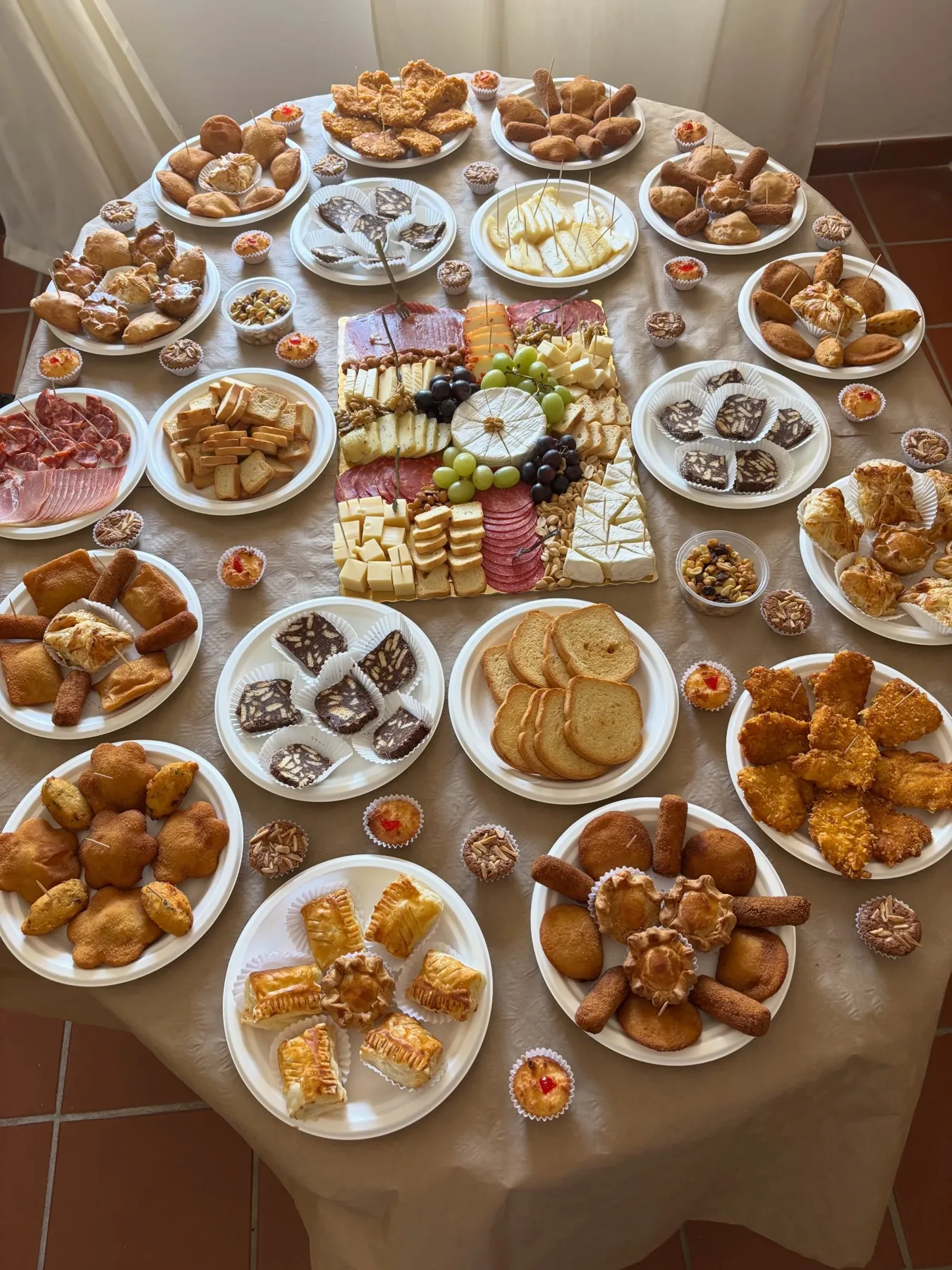 Mesa de festa com dezenas de travessas de salgados, doces e uma tábua de queijos